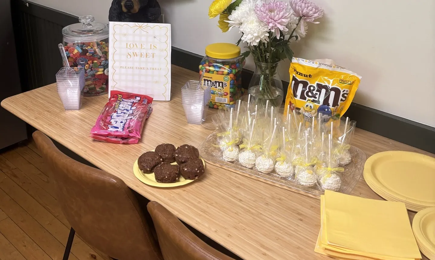 A sweets table with a candy jar, cake pops and a “Love is Sweet” sign